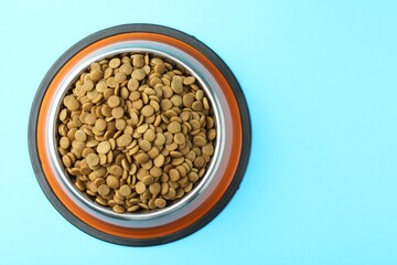 Dry pet food in feeding bowl on light blue background, top view. Space for text