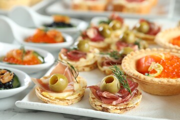 Many different tasty canapes on white marble table, closeup