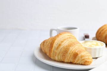 Tasty fresh croissant served with butter and cup of drink on white tiled table, closeup. Space for text