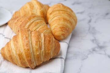 Tasty fresh croissants on white marble table, closeup. Space for text