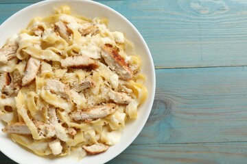 Tasty Alfredo pasta with chicken on light blue wooden table, top view. Space for text