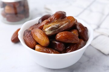 Tasty dried dates in bowl on white marble table, closeup