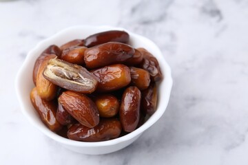 Tasty dried dates in bowl on white marble table, closeup. Space for text