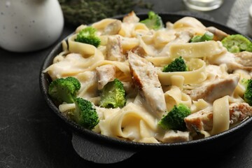 Delicious pasta Alfredo with chicken, cheese, creamy sauce and broccoli on black table, closeup