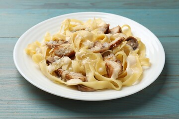 Tasty Alfredo pasta with chicken and mushrooms on light blue wooden table, closeup