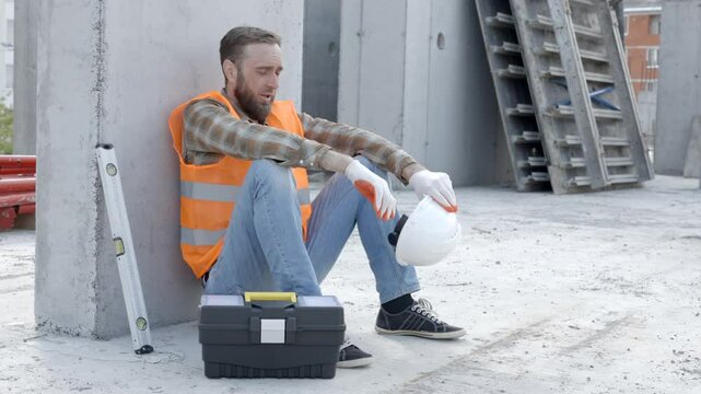 Builder repairman, foreman in safety helmet and vest sitting down to rest at workplace in building next to tool box and ruler