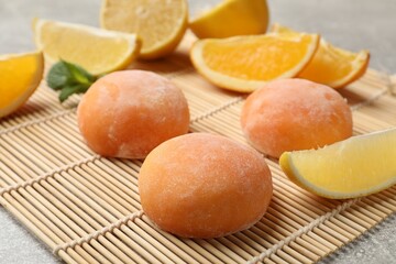 Bamboo mat with tasty mochi, cut orange, lemon and mint on grey textured table, closeup