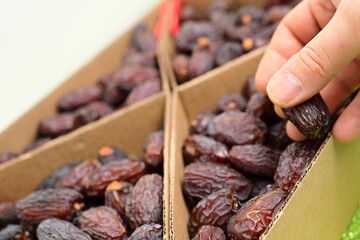 Hand Selecting Fresh Dates from Box. Close-up of a hand picking fresh, ripe dates from a box, showcasing healthy dried fruit in a natural setting.

