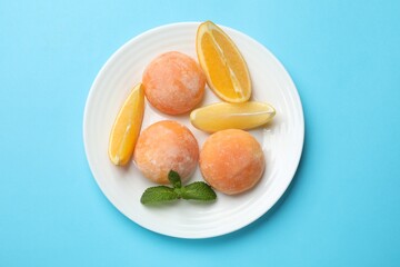Plate with tasty mochi, cut orange and mint on light blue table, top view