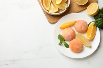 Plate with tasty mochi, cut orange, lemon and mint on white marble table, flat lay. Space for text