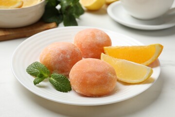 Plate with tasty mochi, cut orange, lemon and mint on white table, closeup