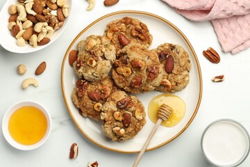 Tasty cookies with nuts, honey dipper and milk on white table, flat lay