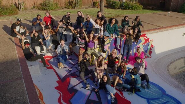 A large group of super hip people sit inside of a drained pool as they look at the camera and smile.
