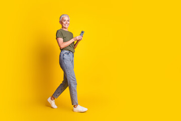 Full length photo of adorable lovely woman wear khaki t-shirt walking chatting modern device empty space isolated yellow color background