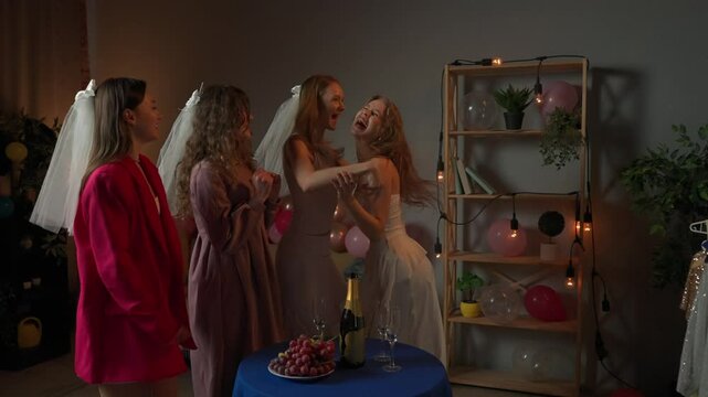 Group of young women friends celebrating bachelorette party at home, bridesmaids meeting the bride at party, smiling and hugging, excited happy expression. Slow motion.