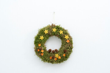 Adventkranz aus Moos mit Sternchen aus Bienenwachswaben und getrockneten Orangenschalen und Lärchenzapfen fertig dekoriert, an der Wand hängend.