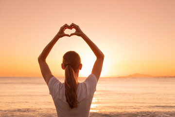 Young female making heart shape on beautiful sunset ocean background. I love nature concept 
