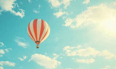 Fototapeta premium A colorful hot air balloon floats peacefully in a bright blue sky filled with fluffy clouds and warm sunlight.
