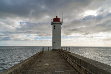 Le phare du Raoulic, entouré des pavés du môle, se dresse fièrement sous un ciel nuageux...
