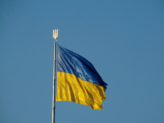 A rectangular flag of blue top and yellow bottom colors, flying on a metallic pole against a clear sky