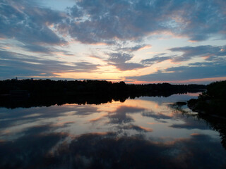 A tranquil sunset over a calm, reflective body of water with scattered clouds and potential vegetation on the shoreline The colors range from warm oranges to cool blues, capturing a moment just afte