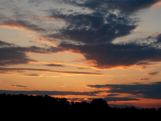 Sunset scene with vibrant orange and yellow sky, dark clouds contrasting, horizon line visible in lower right corner, overall composition evoking calmness