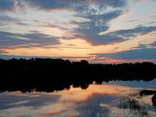 Obraz premium A tranquil sunset scene over a lake, with trees flanking the sides The vibrant sky, reflecting on the calm water, creates a mirror effect