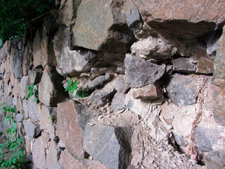 Close-up view of an old, irregular stone structure, possibly part of a larger building The stones are closely stacked, with vegetation growing in the cracks and showing signs of weathering Natural