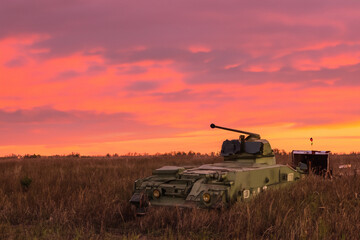 Fototapeta premium Large tank sits on the grass in front of red sky. A field of tanks at sunset in the evening. A green field with a transport tank at sunset. A green field of tanks at sunset with green lifestyle.