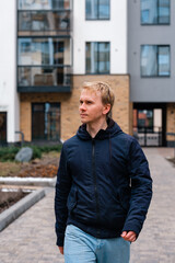 A Caucasian man in a jacket walks along the street along the houses