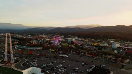 A 4K golden hour drone shot moving backward over Pigeon Forge, Tennessee, during sunset. The wide view highlights the Ferris wheel in the distance, framed by a scenic landscape.