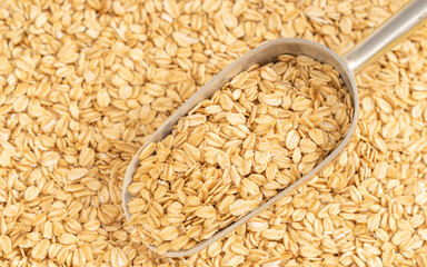 Metal scoop filled with rolled oats on a scattered oat background. Ideal for healthy food and natural living themes.