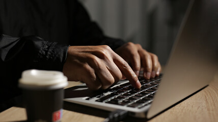 Programmer writing code on laptop keyboard at night