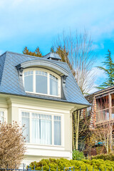 Top of grey stucco luxury house with shingle roof, red and yellow trees and nice windows in Summer in Vancouver, Canada, North America. Day time on June 2024.