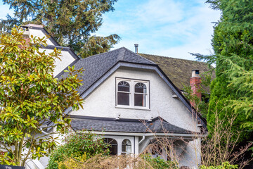 Top of grey stucco luxury house with shingle roof, red and yellow trees and nice windows in Summer in Vancouver, Canada, North America. Day time on June 2024.