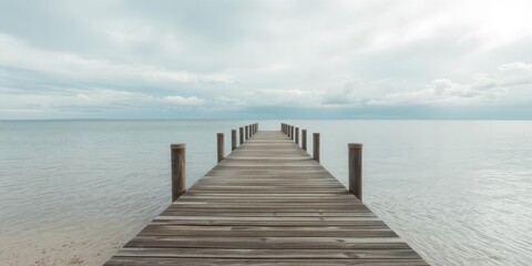 Obraz premium Empty wooden pier stretching out towards calm sea under a cloudy sky, calm, empty