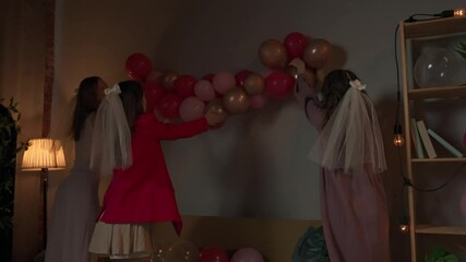 Group of young women friends and bride celebrating bachelorette party at home, bridesmaids decorating party room with colorful air balloons.