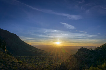 A breathtaking sunset over a desert landscape, featuring rolling hills, Saguaro cacti, and a dramatic sky. The serene setting radiates tranquility and natural beauty.