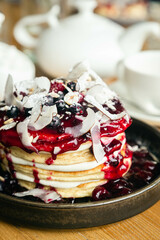 Appetizing vanilla pancakes with fresh berries, hazelnuts, coconut and jam close-up in a cafe, delicious breakfast.