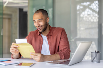 A cheerful man opening and reading an envelope at his office desk. He appears pleased with the contents, symbolizing success, important news, or professional correspondence in a lively workspace.