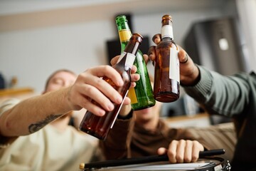 Close up of beer bottles raised in toast with sports fans cheering while watching game at home,...