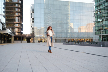 Confident woman walking in urban setting holding laptop