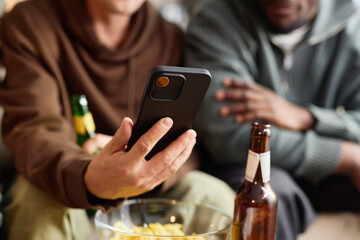 Close up of male hand holding smartphone with three friends looking at screen and drinking beer, copy space