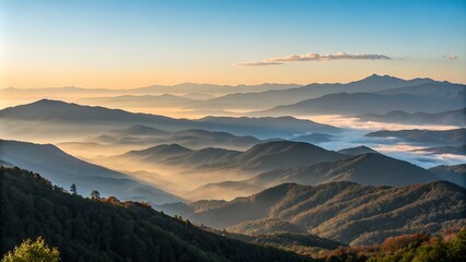 Obraz premium Majestic mountain range during sunrise with glowing golden light, misty valleys, and clear blue sky, showcasing the beauty of nature in vivid detail