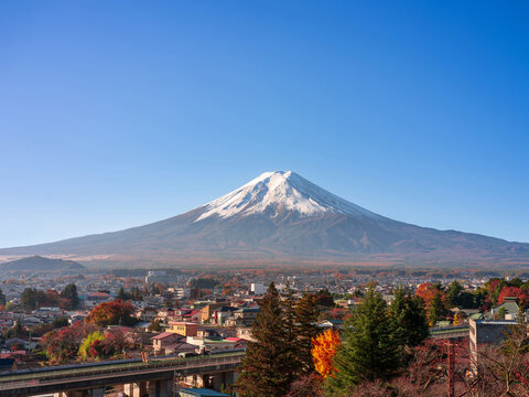 Fujiyoshida, Japan - November 21 2024: Looking up at snow capped mt fuji from the small town with honcho street and traditional japanese buildings and shops. Cool autumn weather with glowing sunlight