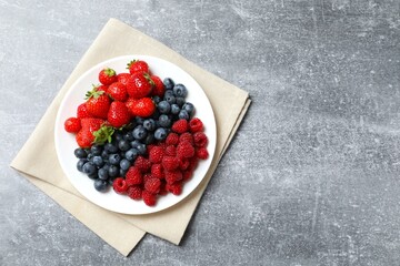 Different fresh ripe berries in bowl on wooden table, top view