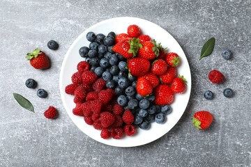 Different fresh ripe berries in bowl on wooden table, top view