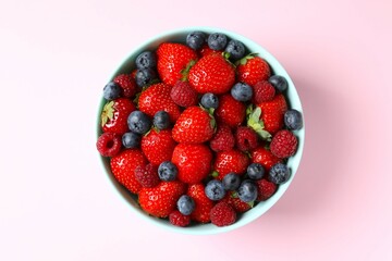 Different fresh ripe berries in bowl on wooden table, top view
