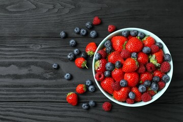 Different fresh ripe berries in bowl on wooden table, top view
