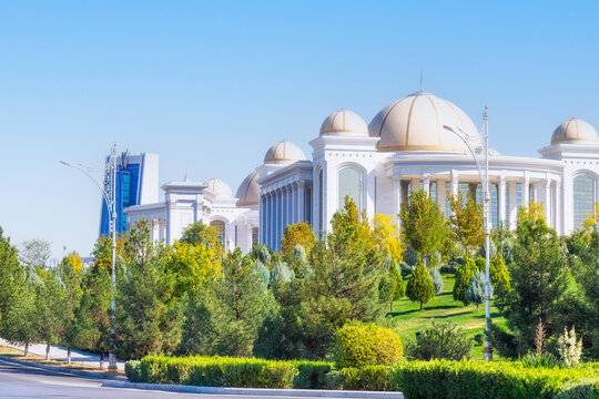 Turkmenistan capital street view with lush green park s and white marble  buildings behind greenery  under a clear blue sky. Ashgabat